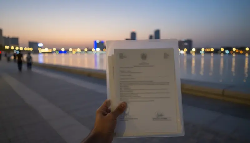Certificates in a folder by the Sharjah waterfront at dusk